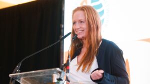 Red haired woman talking into a microphone while presenting and smiling