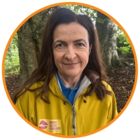 Brown haired woman in a yellow jacket and blue scarf smiling in front of some trees. Michelle Boyle Tourism Manager Newry Mourne & Down District Council.