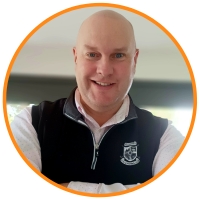 Bald man smiling with arms crossed and wearing a white shirt and navy vest