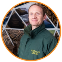 Red haired man smiling in front of a coloured octagon structure and wearing green jacket with a collar