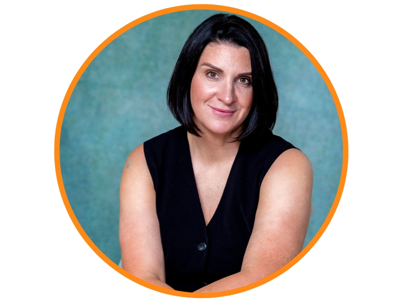 Brown haired woman smiling with their arms crossed on their legs and wearing a black shirt